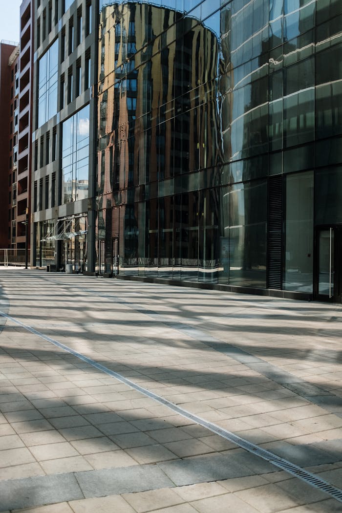 A urban scene showcasing a modern building with reflective glass facade and empty pavement.