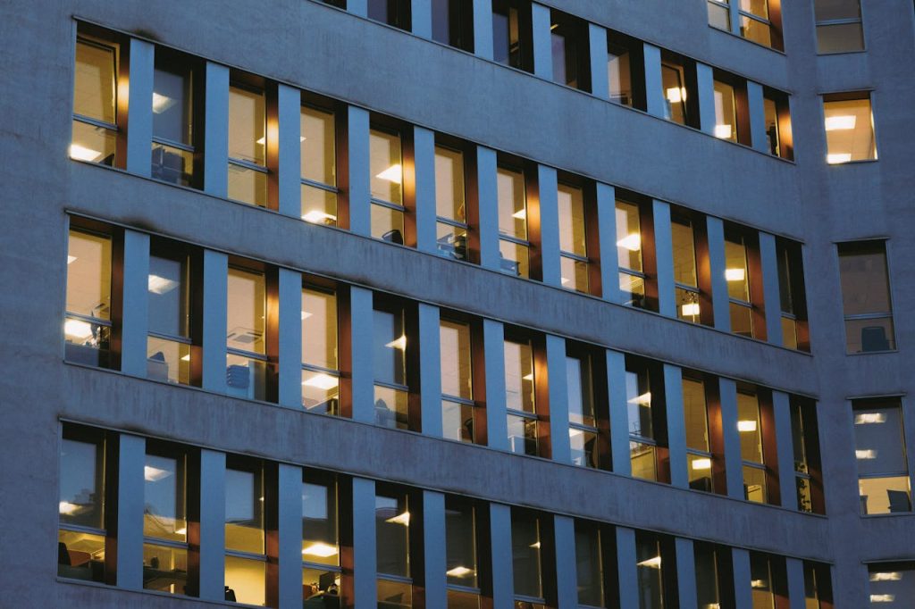 pexels photo 9741490 Exterior view of a modern office building with illuminated glass windows during dusk, showcasing urban architecture.